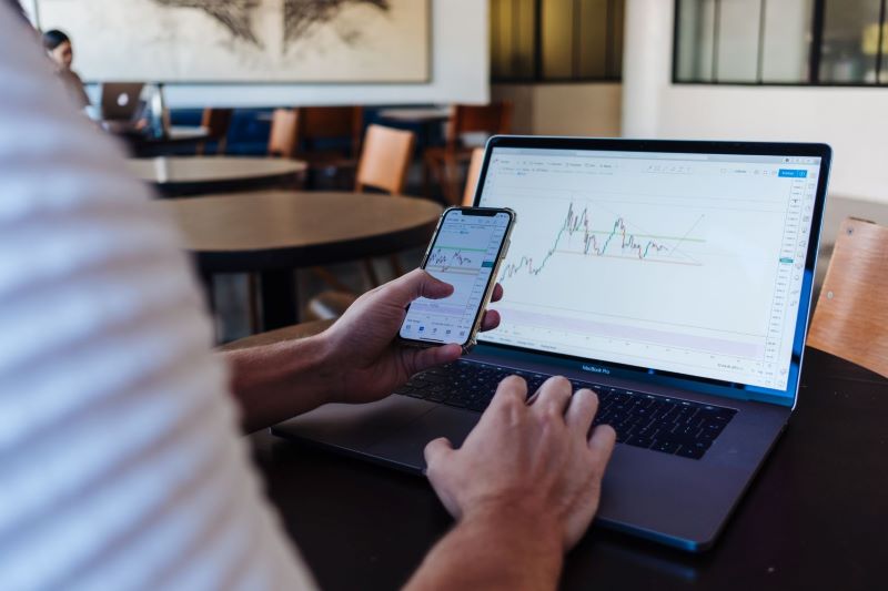 Man with phone in business attire checks stocks against computer screen