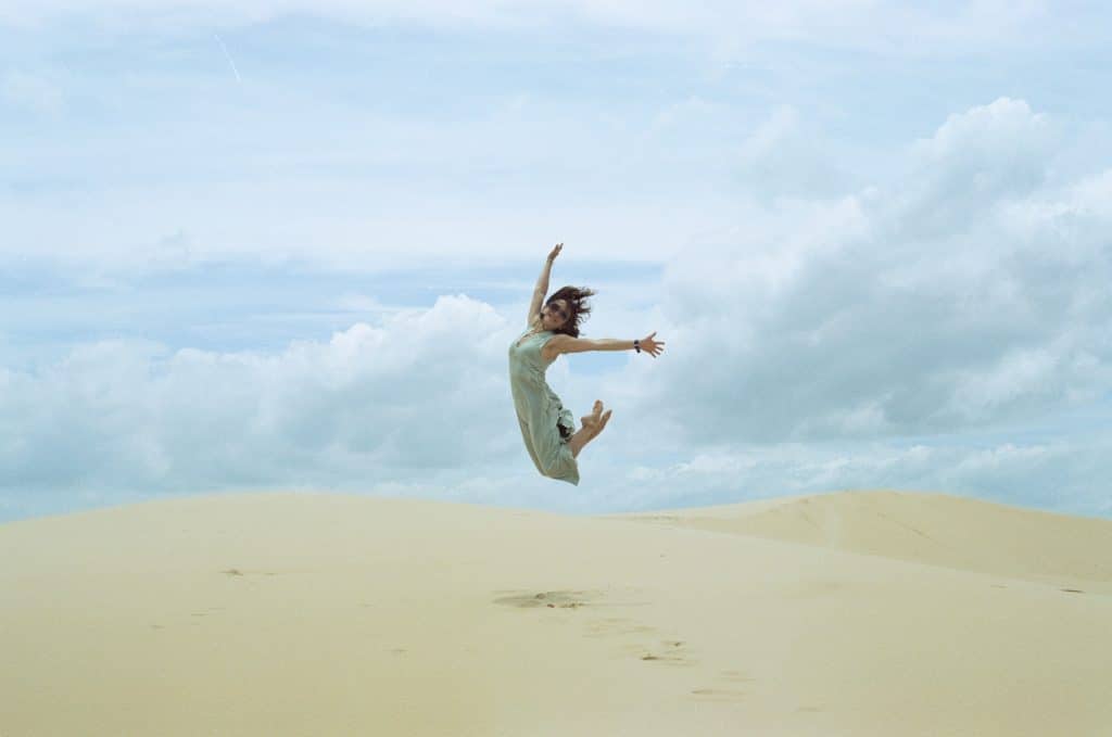 Woman jumping in the air on beach against clouds, positive fresh start