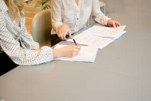 Close up, two women in formal attire at a table, signing important documents, slanted composition