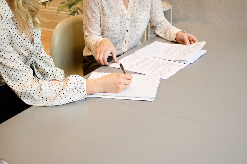 Close up, two women in formal attire at a table, signing important documents, slanted composition
