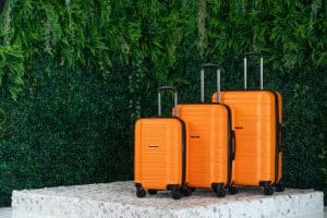 Three orange suitcases of different sizes with greenery in the background.