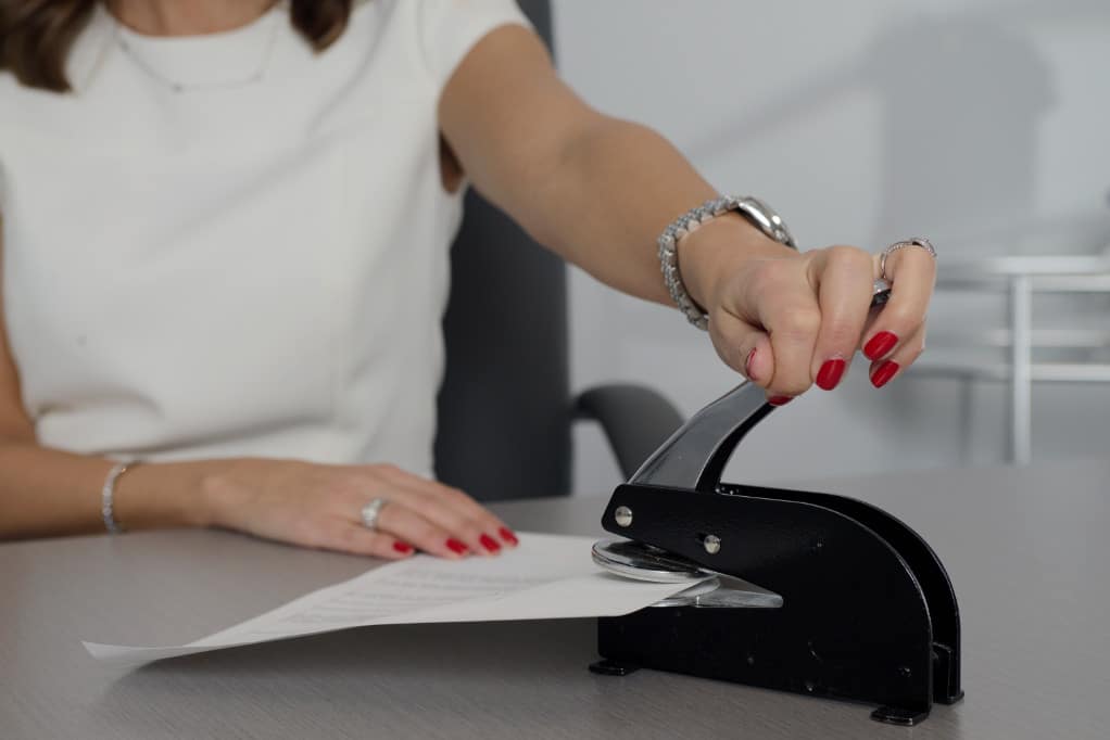 Woman in business setting with silver watch and manicured nails stapling documents, filing taxes international divorce