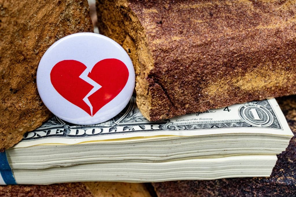 Badge with a broken heart resting on piles of dollars against bricks