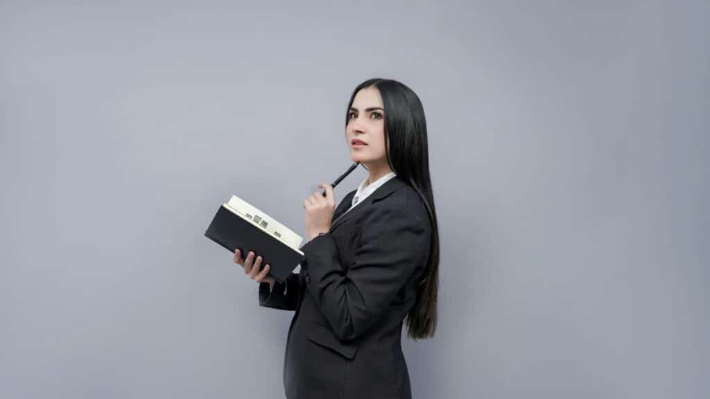 Woman in business suit with long dark hair reflects on divorce mediation while holding bound notebook and pen