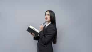 Woman in business suit with long dark hair reflects on divorce mediation while holding bound notebook and pen